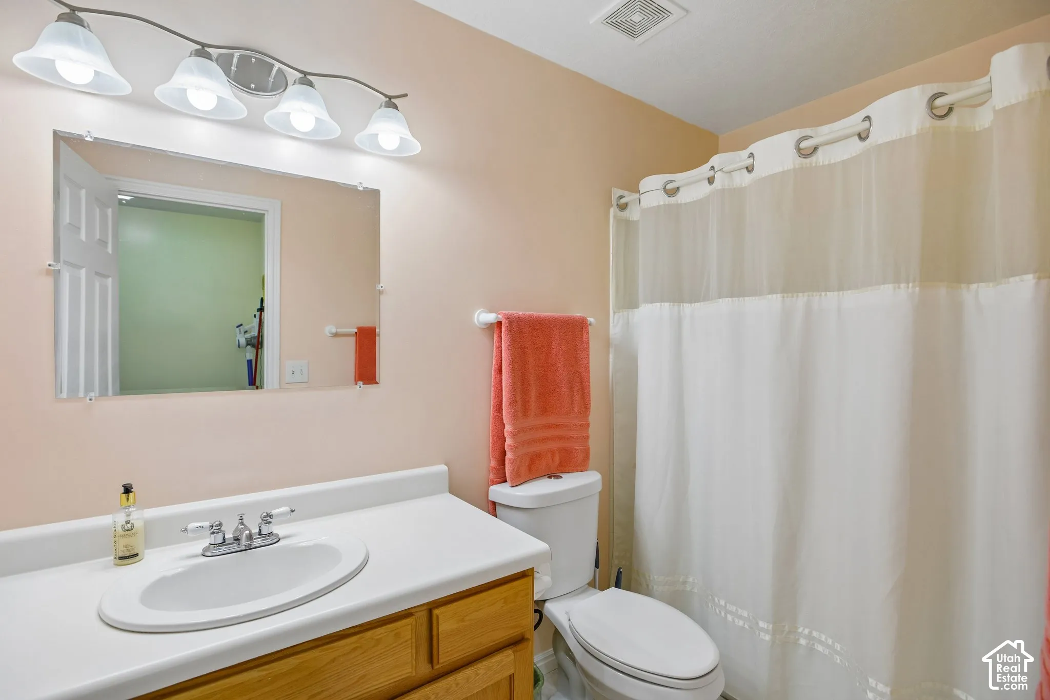 Bathroom featuring a vanity with a wood-finish base and white countertop, an oval undermount sink with a chrome faucet, and a wall-mounted mirror