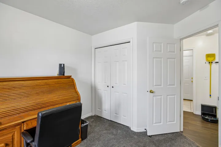 Interior room with neutral wall paint, gray carpeting, a bi-fold closet door, and a paneled door leading to an adjacent space with wood-finish flooring