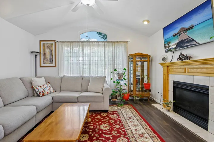 Vaulted ceiling living area featuring wood-finish flooring, a contemporary ceiling fan, and an arched window