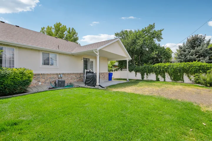 Expansive backyard featuring a manicured lawn, a covered patio, and a white privacy fence with mature vine coverage