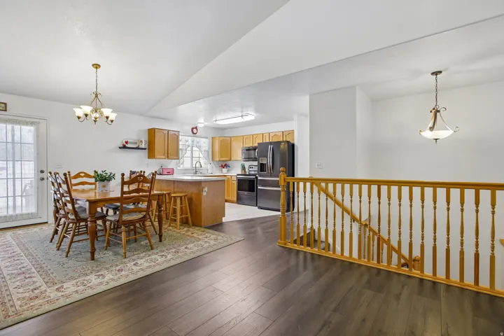 Open-concept living space featuring wood-finish flooring, a wood banister, and a kitchen with light wood cabinetry and dark appliances