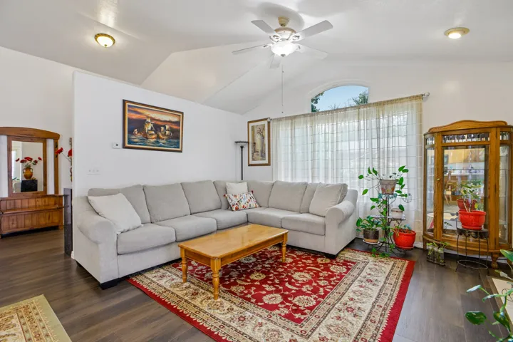 Living area featuring vaulted ceilings, wood-finish flooring, a ceiling fan, and large windows with an arched transom
