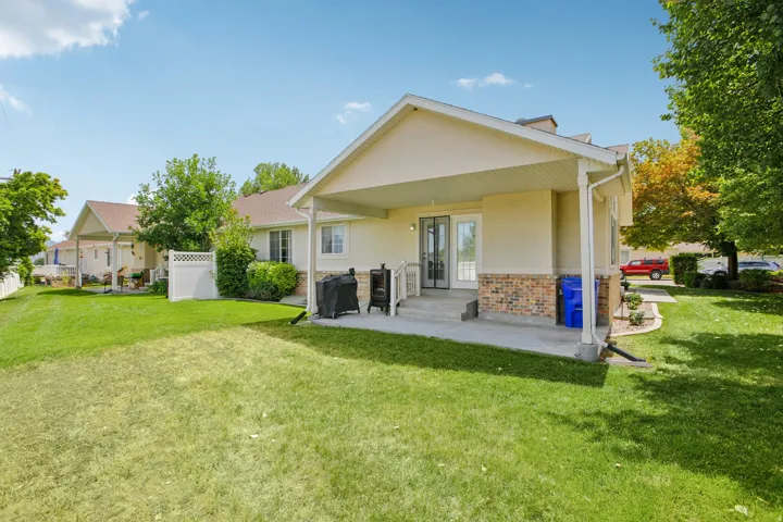 Expansive backyard featuring a manicured lawn, covered patio, white vinyl fencing, brick veneer detailing, and mature trees