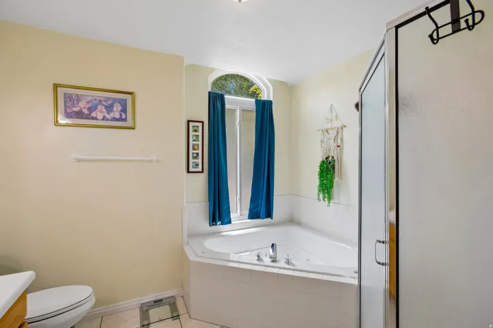 Jetted corner tub with tile surround, framed by an arched window