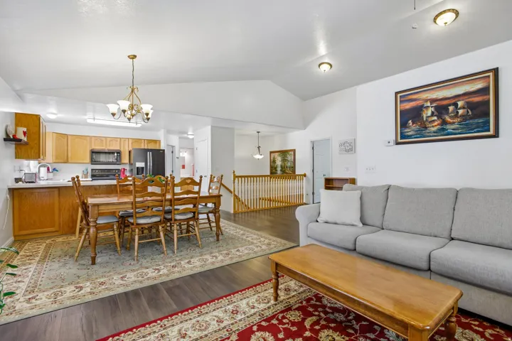 Expansive open-concept living area featuring high vaulted ceilings, wood-finish flooring, and a kitchen with light wood cabinetry and dark appliances