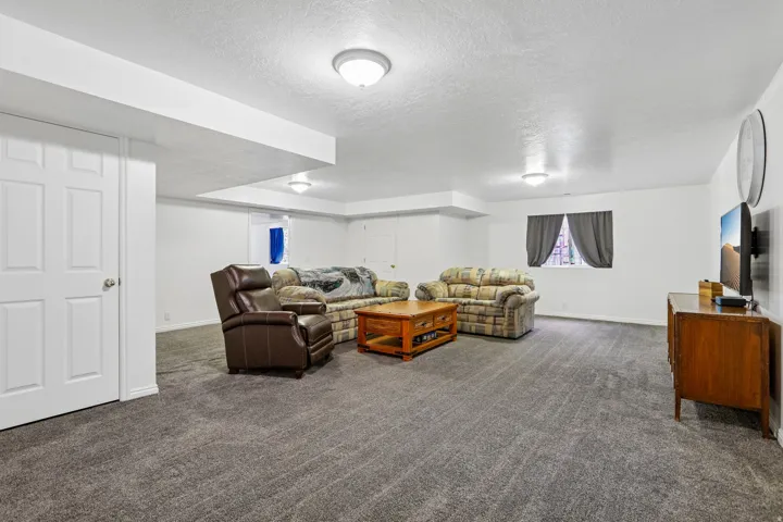 Open living area featuring plush gray carpeting, white painted walls, and ceiling-mounted lighting
