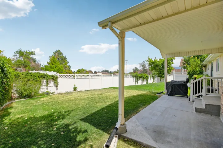 Expansive rear yard featuring a covered patio, concrete surface, and white vinyl fencing