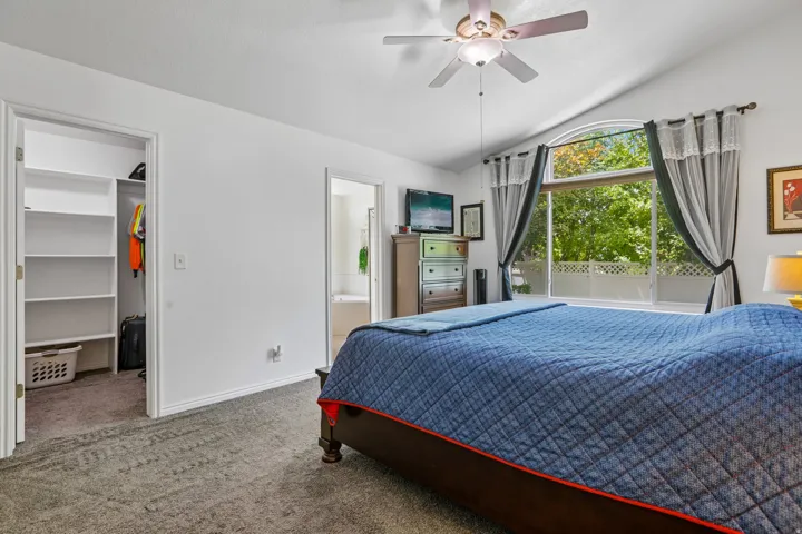 Carpeted bedroom featuring a vaulted ceiling and a ceiling fan with integrated lighting