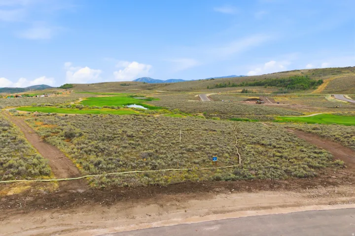 Expansive undeveloped lot with natural landscaping, a paved road, and distant green areas with water features