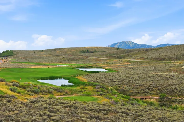 Expansive golf course landscape featuring a manicured green, multiple water features, and distant mountain scenery