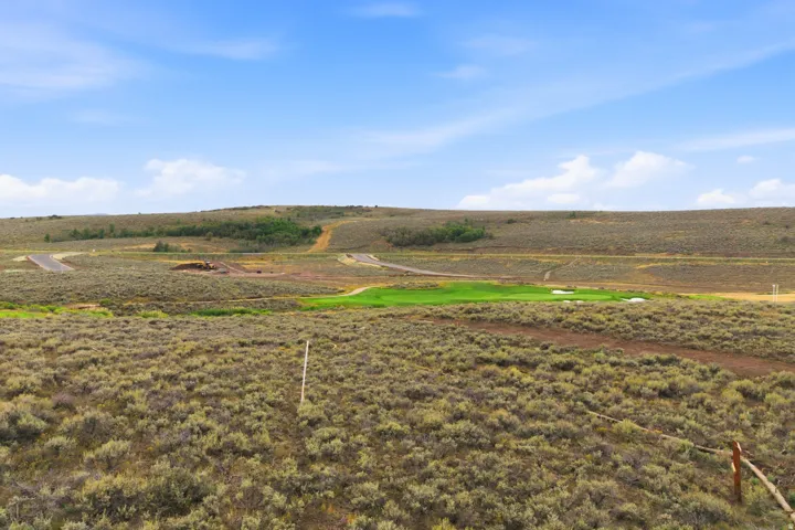 Expansive open land with natural shrubbery and distant green golf course elements