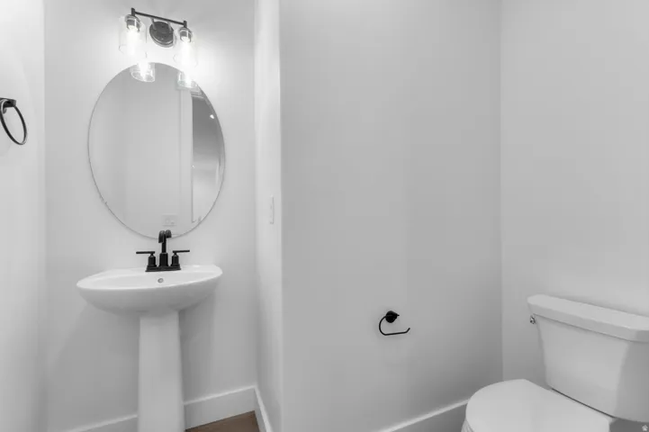 Pedestal sink with a matte black faucet, oval mirror, and a three-light vanity fixture