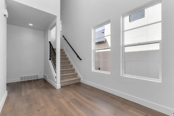 Wood-finish flooring, staircase with carpet treads, black metal balusters, and white walls with recessed lighting
