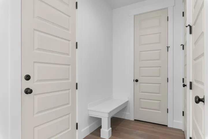 Built-in white bench, wood-finish flooring, and paneled doors with matte black hardware