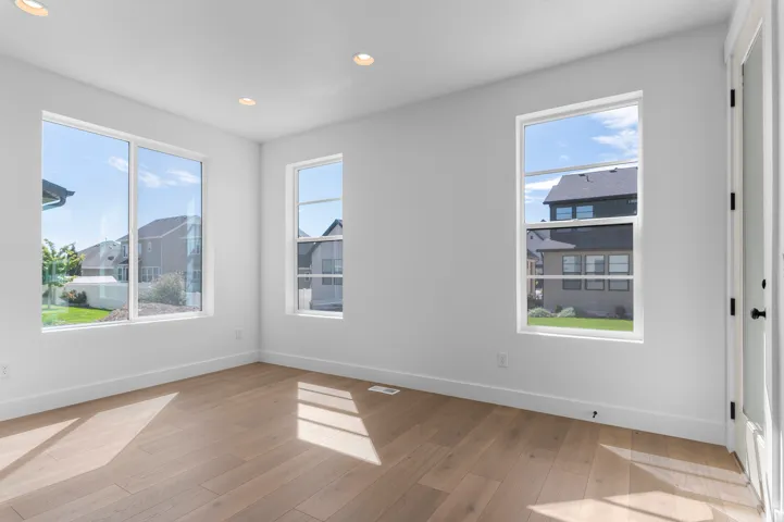 Recessed ceiling lighting, wood-finish flooring, white walls, multiple windows, and a white interior door