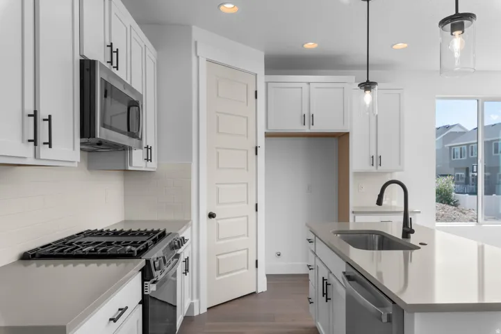 White cabinetry with matte black hardware, stainless steel microwave, gas range, light-toned countertops, and an undermount sink with a black faucet