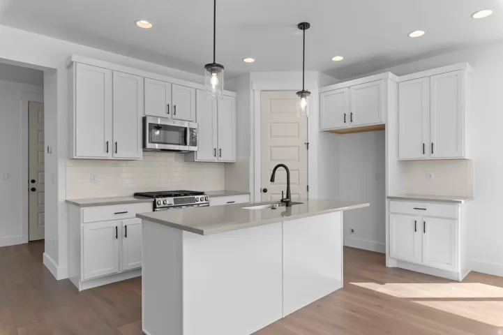 Wood-finish flooring, white cabinetry, island with sink, stainless steel appliances, and recessed lighting