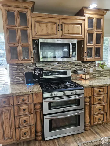 Kitchen featuring wood-finish cabinetry, stainless steel double oven range, stainless steel microwave, stone countertops, and a tiled backsplash