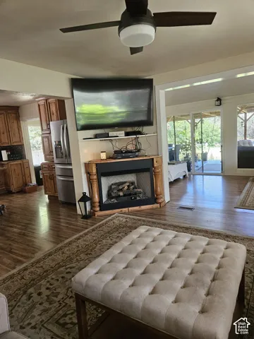 Living area with wood-finish flooring featuring a built-in fireplace with a decorative mantel and a ceiling fan
