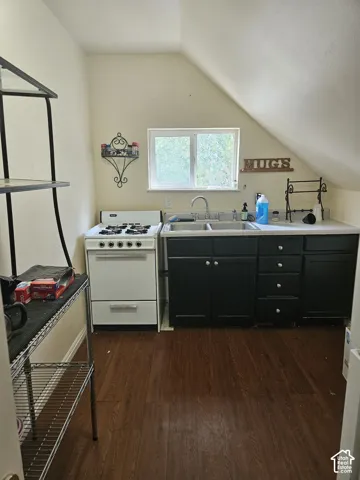 Compact kitchen featuring a white gas range, dark wood-finish flooring, a double basin sink, black base cabinetry, and a white countertop