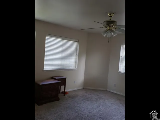 Carpeted room featuring a ceiling fan with integrated lighting, two windows with horizontal blinds, and neutral wall paint