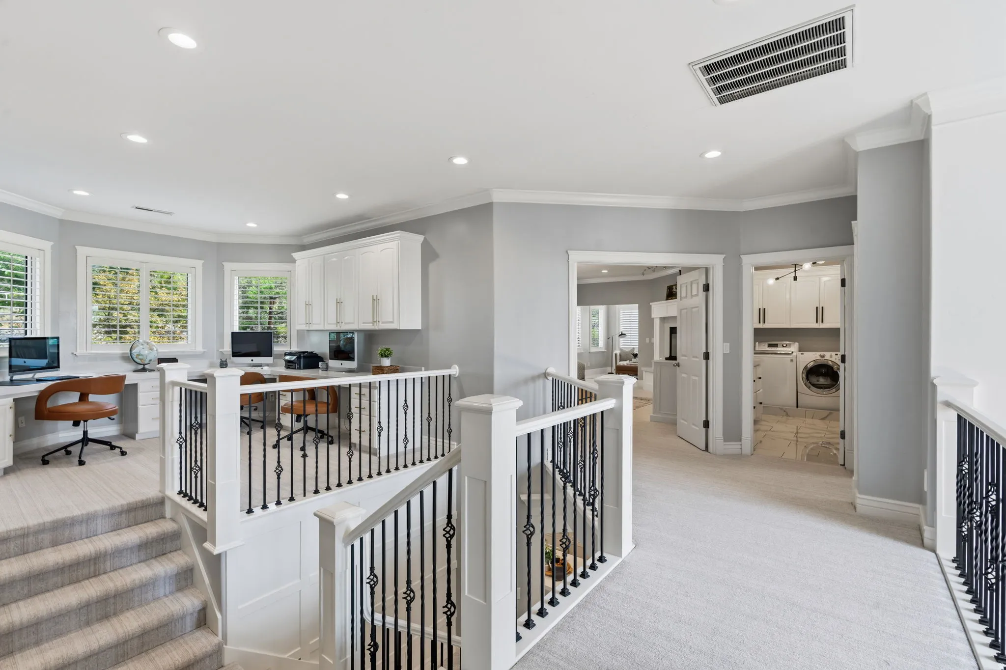 Carpeted hallway leading to an office space with multiple windows, built-in cabinetry, and 3 outward facing integrated desks.  Perfect for homework!