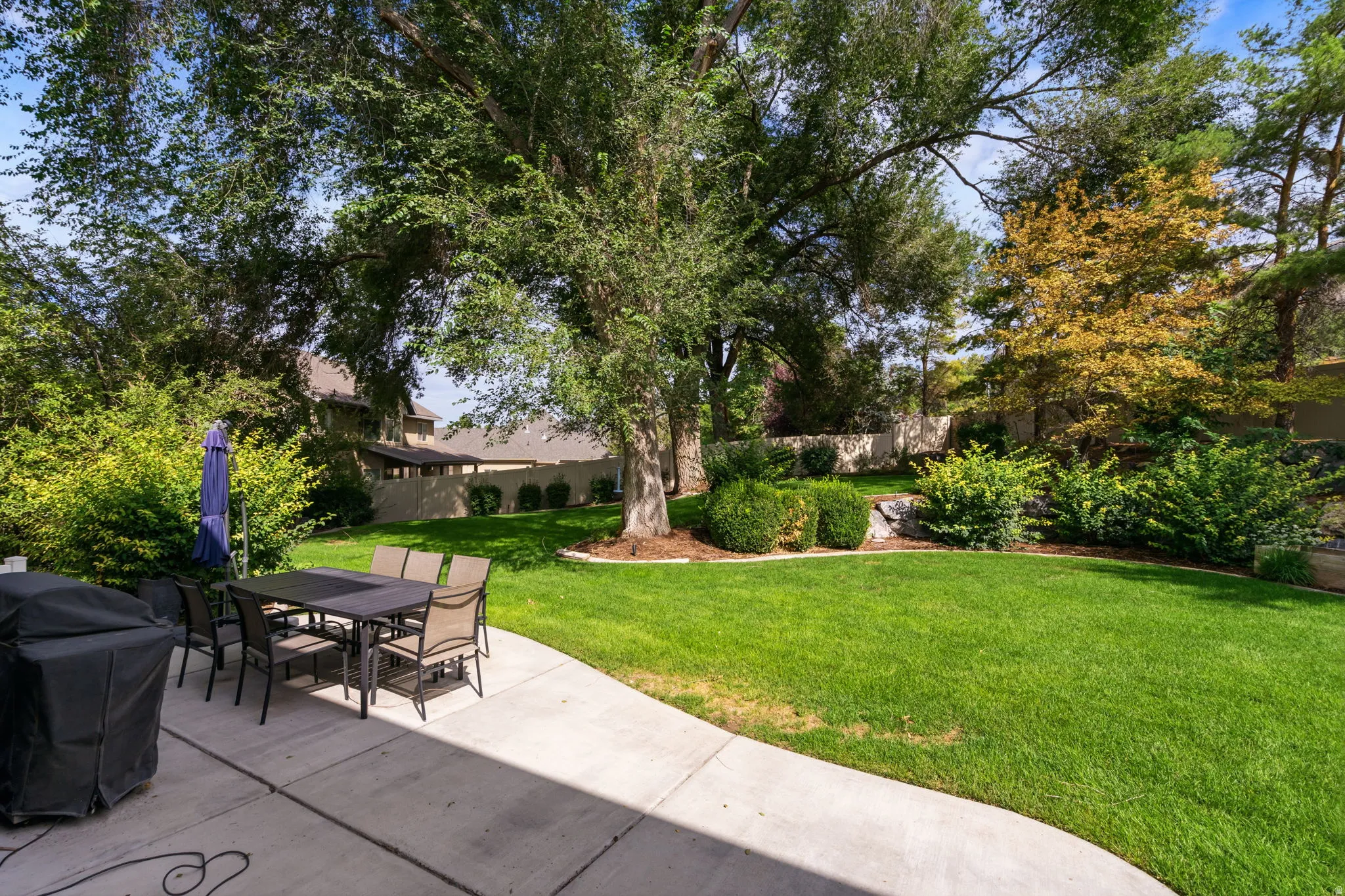Expansive backyard featuring a lush lawn, mature trees, concrete patio, and landscaped perimeter with shrubbery.  RV Parking