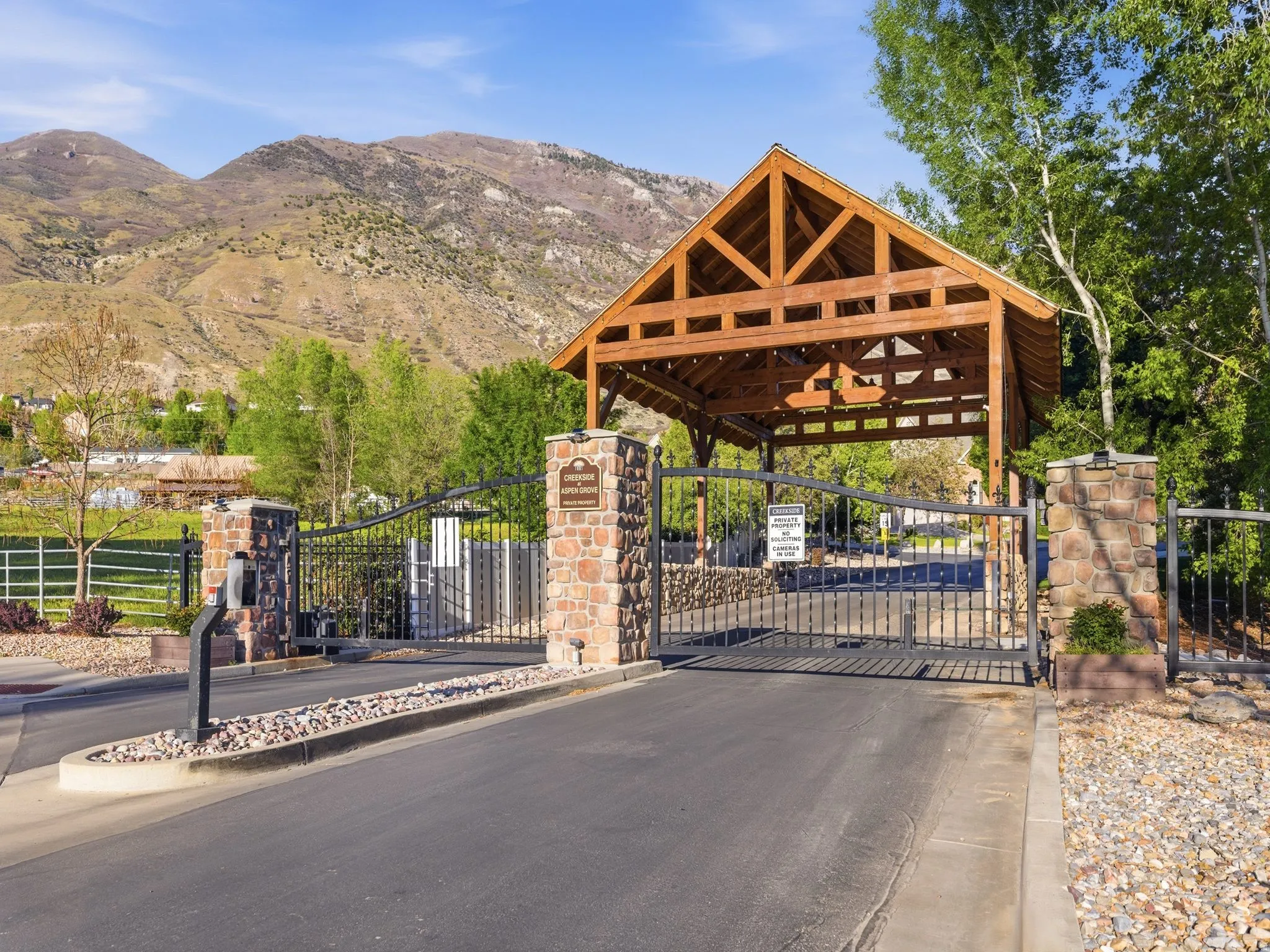 Gated entry featuring a timber-frame canopy, wrought iron gates, and stone pillars