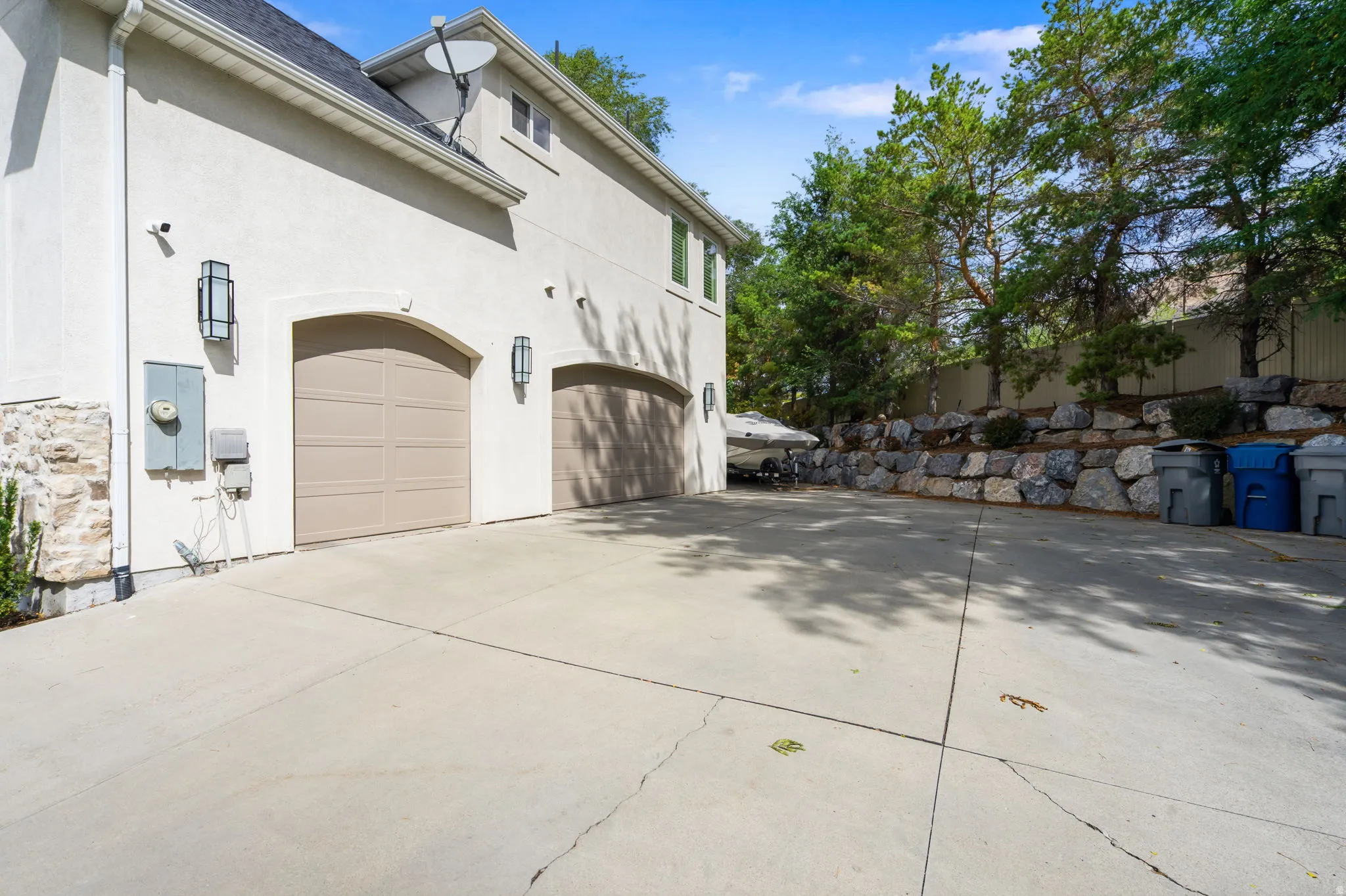 Three-car garage with arched doors, RV parking, stucco exterior, stone facade detailing, and integrated exterior lighting