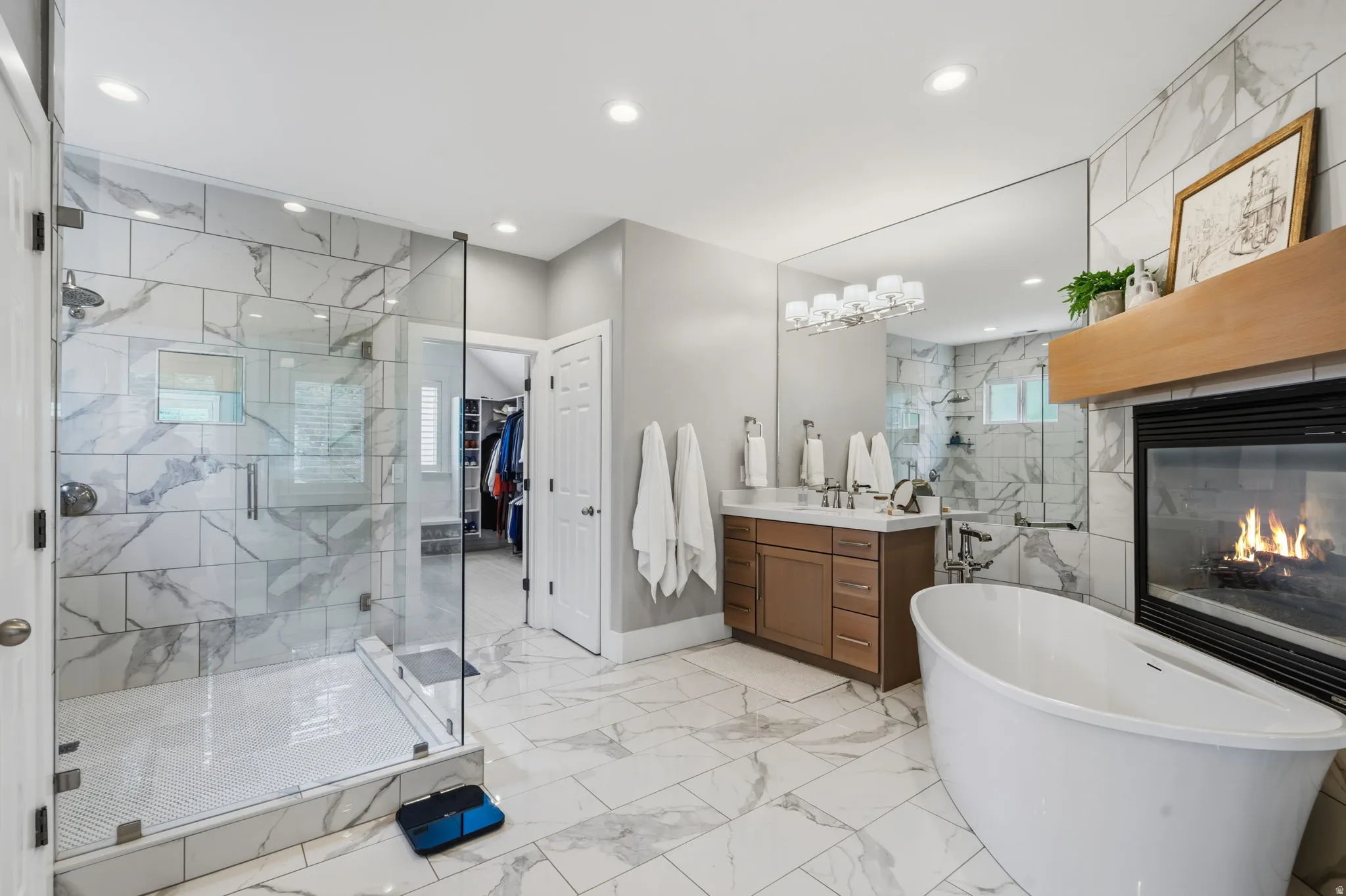 A luxurious, spa-like primary bath finished in marble-look ceramic tile and featuring a large soaker tub positioned beside the two-way glass fireplace-perfect for relaxing in the tub.