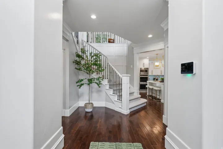 Hardwood flooring, white painted millwork, carpeted staircase with iron balusters, recessed lighting, and a kitchen entry with custom built-ins