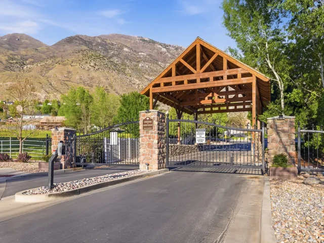 Gated entry featuring a timber-frame canopy, wrought iron gates, and stone pillars