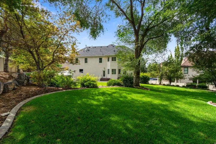 Expansive 2-tiered backyard featuring a manicured lawn, mature trees, a tree swing and a terraced landscape with natural stone accents