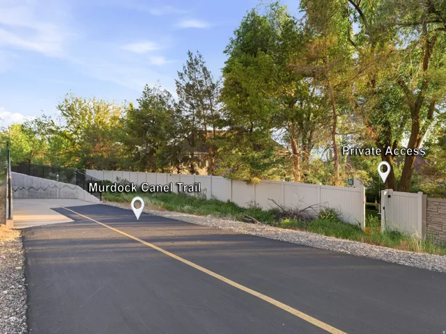 Paved access to the Murdock Canal Trail featuring a white vinyl fence and mature trees