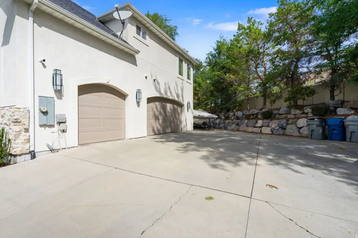 Three-car garage with arched doors, RV parking, stucco exterior, stone facade detailing, and integrated exterior lighting