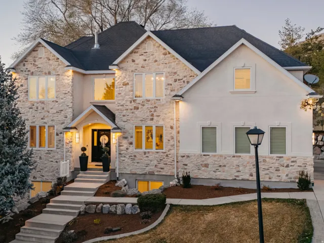 Stone and stucco exterior with multiple windows, tiered concrete walkway, landscaped terracing, and an asphalt driveway