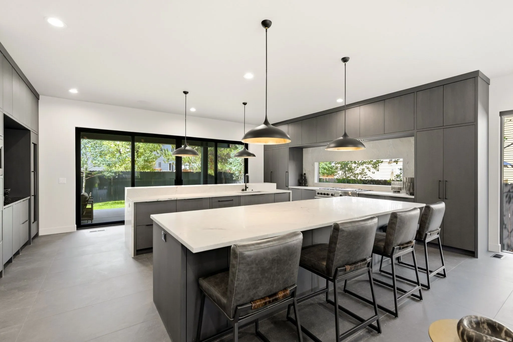 Spacious kitchen featuring two large islands with white countertops, extensive dark wood-finish cabinetry, recessed lighting, and modern pendant lighting fixtures