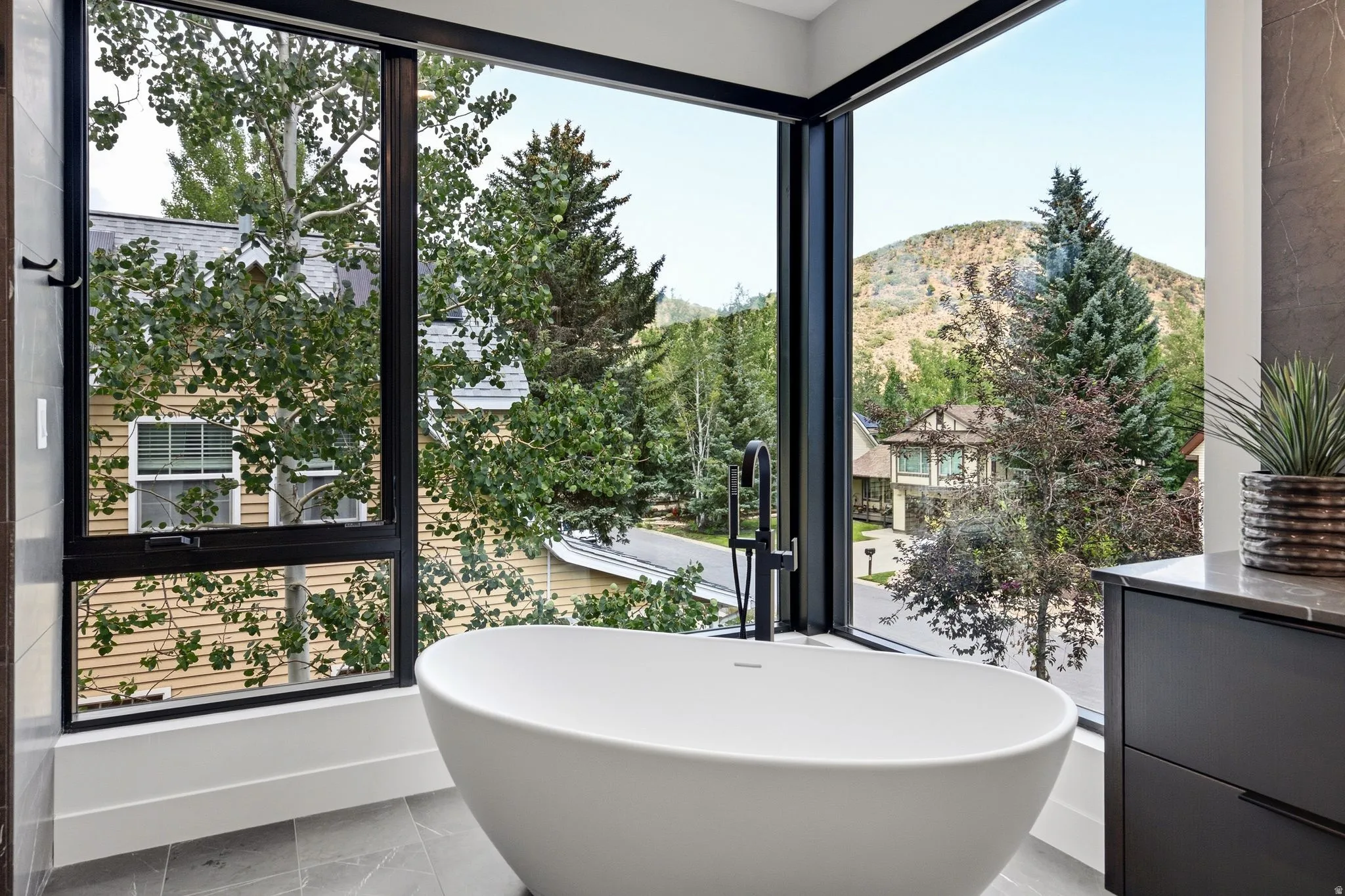 Freestanding soaking tub with a floor-mounted matte black faucet, set against expansive black-framed windows