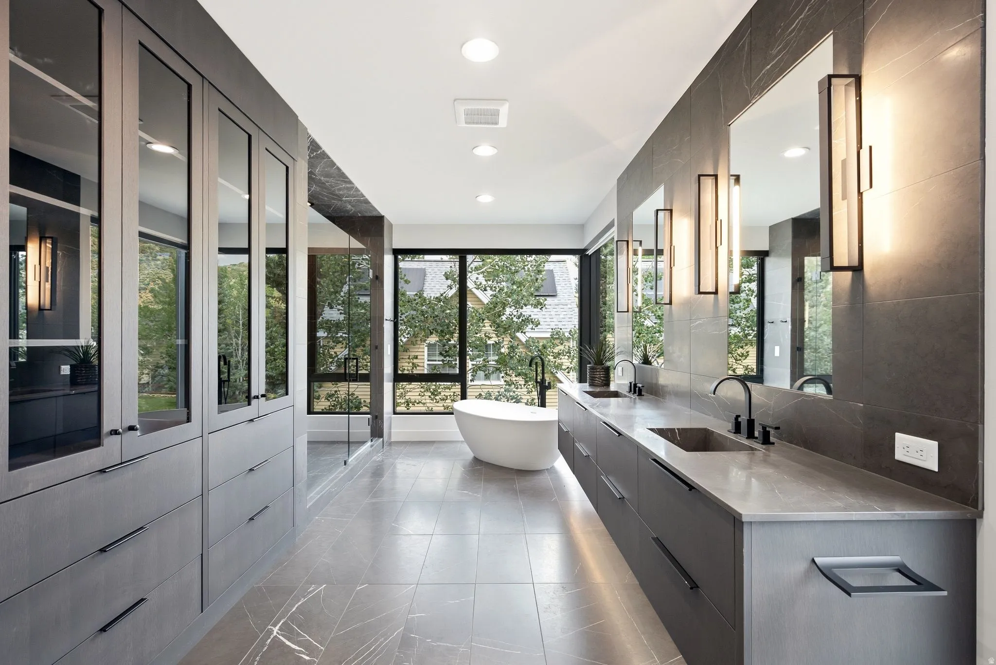 Modern full bathroom featuring a freestanding soaking tub, dual floating vanities with integrated sinks, and ample natural light through large windows