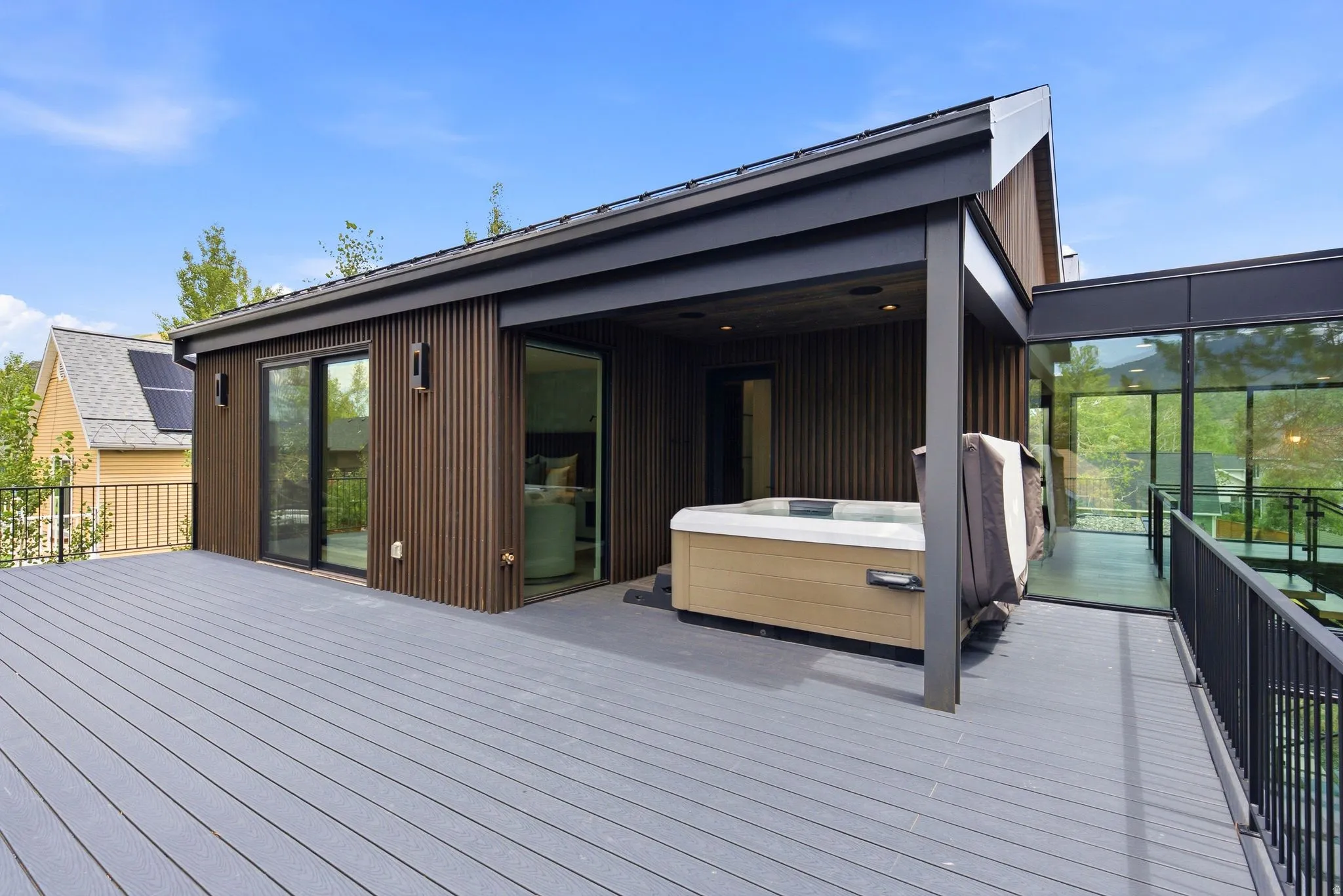 Expansive outdoor deck featuring a built-in hot tub, dark composite decking, and contemporary vertical wood paneling