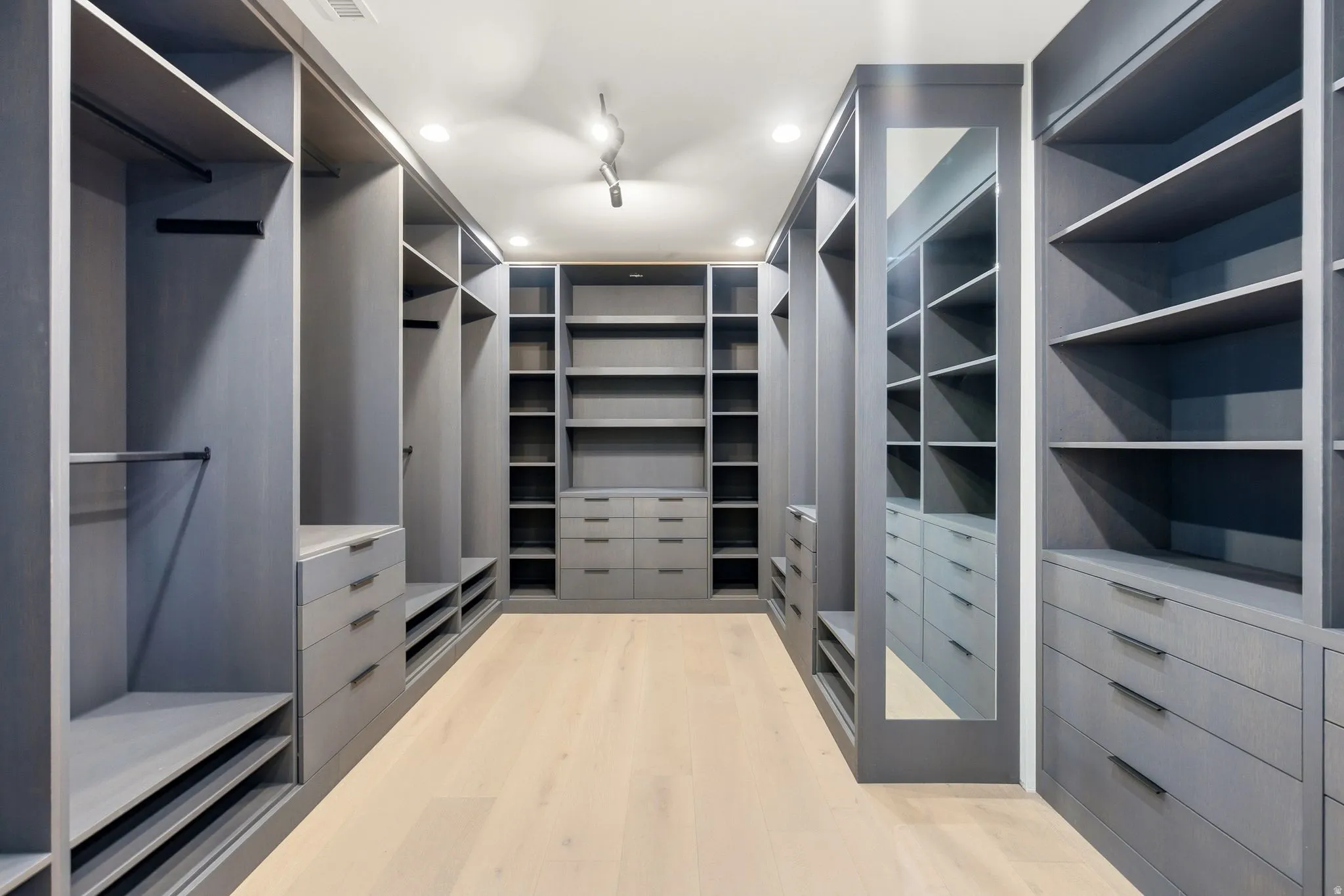 Expansive custom closet featuring extensive built-in cabinetry, integrated shelving, multiple hanging rods, and light wood-finish flooring