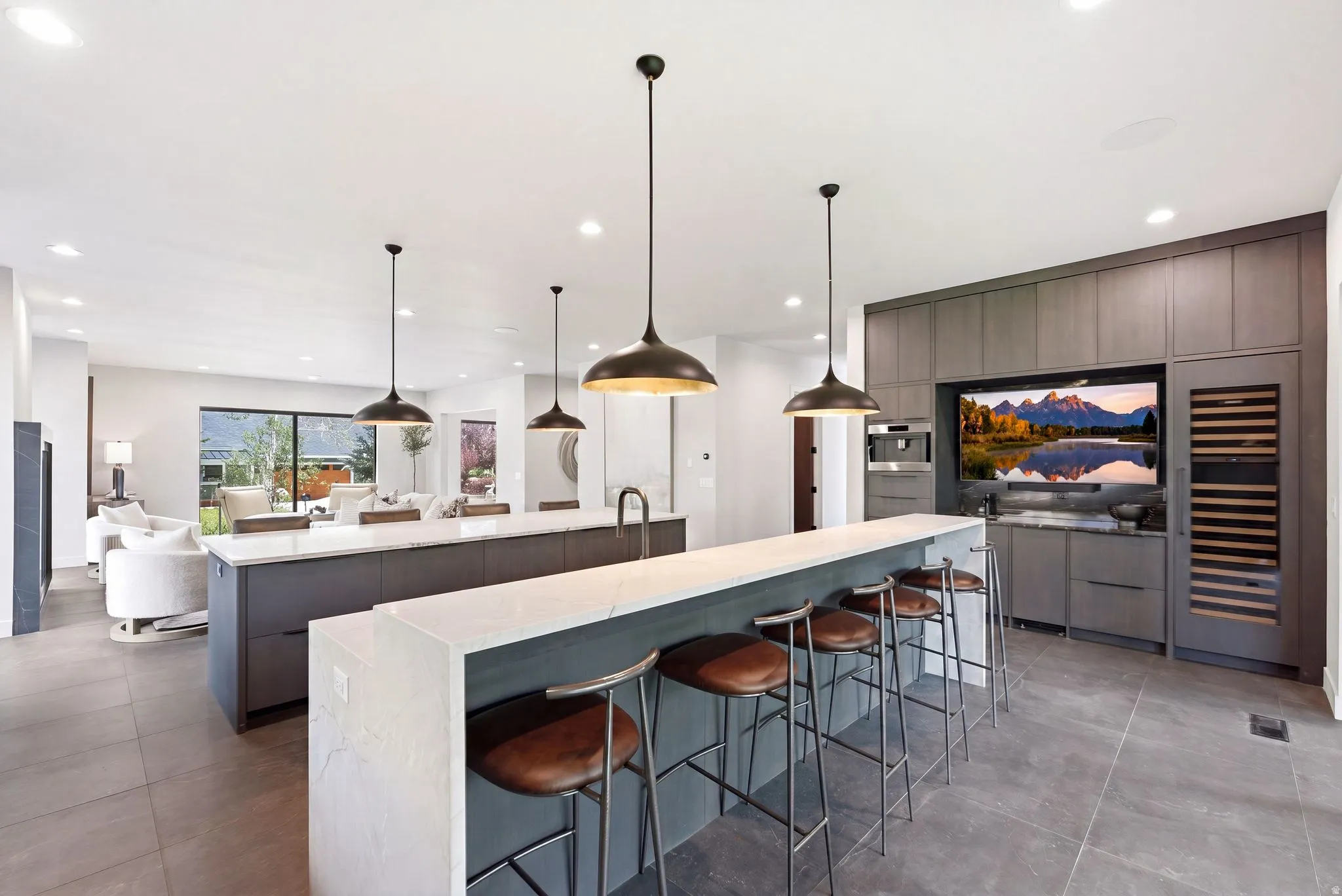 Contemporary kitchen featuring a large waterfall-edge island with seating, a secondary island with an undermount sink, built-in shelving, and dark pendant lighting fixtures