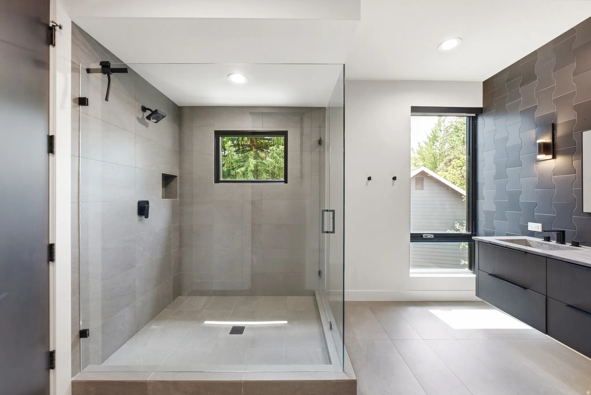 Contemporary bathroom featuring a spacious glass-enclosed shower with matte black fixtures, a built-in shower niche, and light gray tiled walls