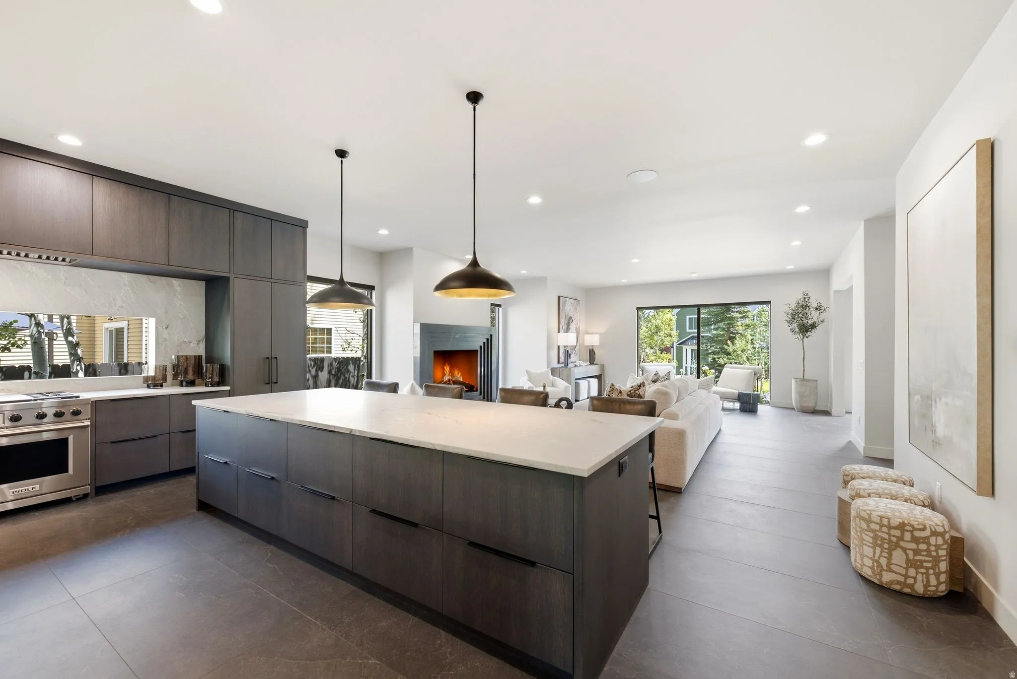 Contemporary kitchen featuring a large center island with a white countertop, dark wood-finish cabinetry, and stainless steel range