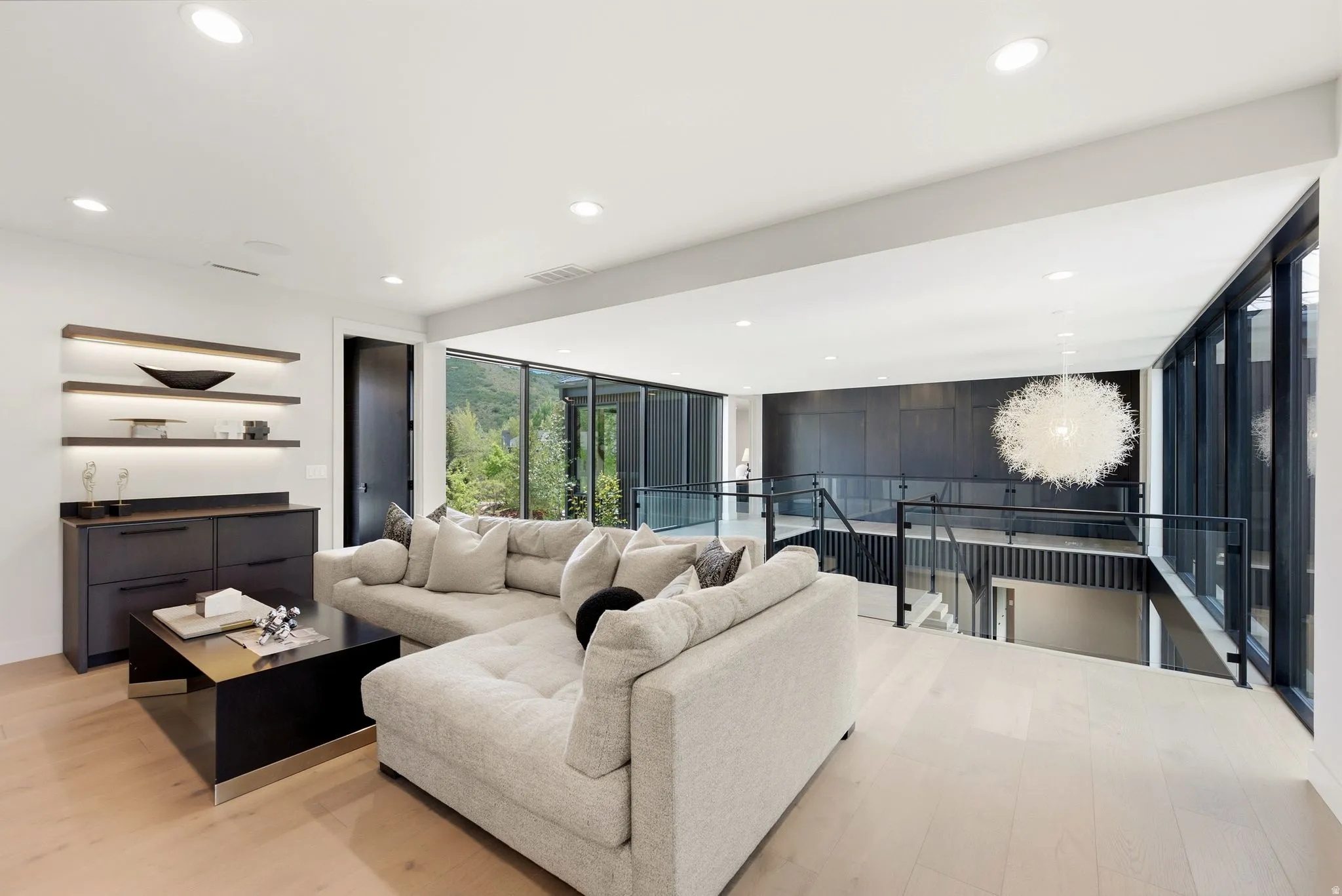 Open concept upper-level living space featuring light wood-finish flooring, recessed lighting, and a modern built-in bar area with illuminated shelving