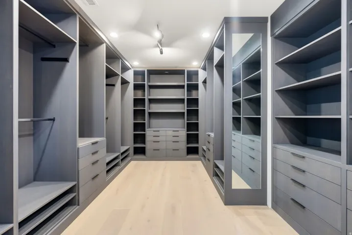 Expansive custom closet featuring extensive built-in cabinetry, integrated shelving, multiple hanging rods, and light wood-finish flooring
