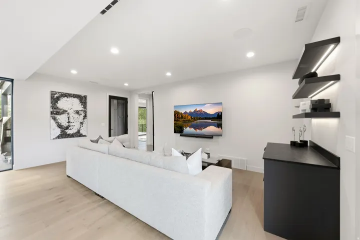 Open-concept living area featuring light wood-finish flooring, recessed lighting, and a mounted flat-screen television