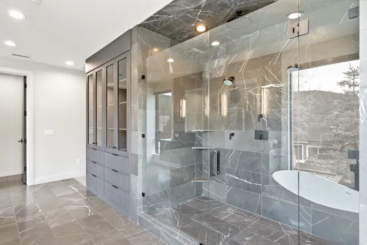 Frameless glass shower enclosure featuring multiple shower heads and a built-in bench