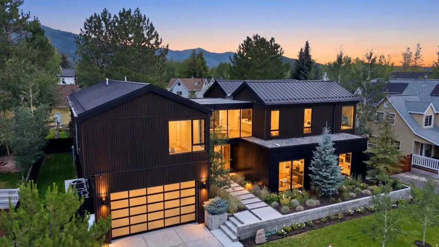 Contemporary black exterior featuring a metal roof, expansive windows, a sectional frosted glass garage door, a stepped concrete walkway, and landscaped garden beds
