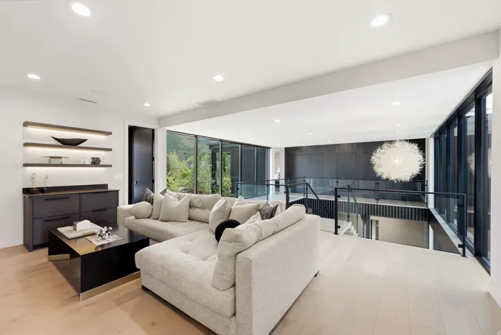 Open concept upper-level living space featuring light wood-finish flooring, recessed lighting, and a modern built-in bar area with illuminated shelving